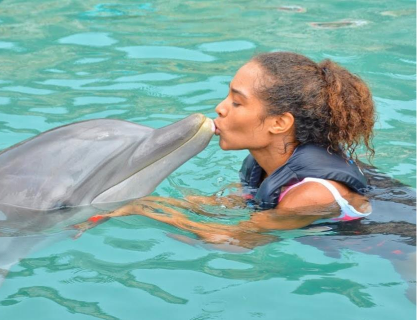 A woman is in a pool embracing a dolphin